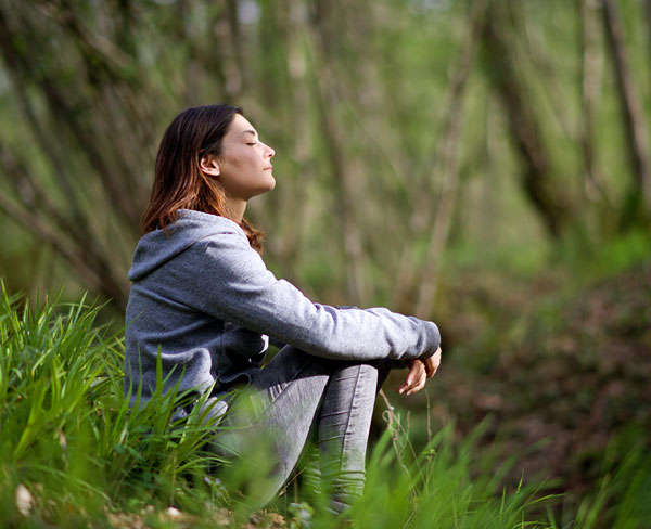 Image of lady sitting in green woods being mindful and relaxed.